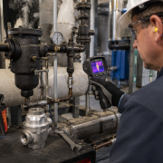 Technician using a thermal camera to inspect a steam trap and valve station for maintenance or replacement needs.